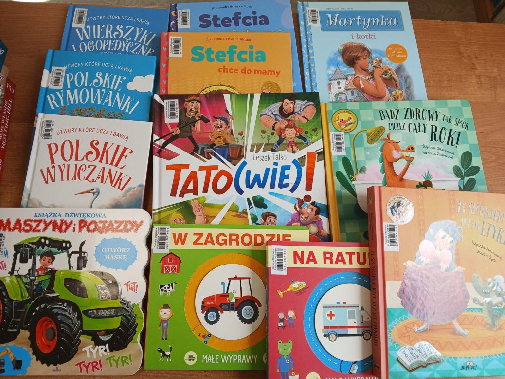 Na zdjęciu znajduje się stos kolorowych książek dla dzieci na drewnianym tle. Okładki mają żywe kolory i różnorodne ilustracje. Każda książka przedstawia różne tematy i postacie.