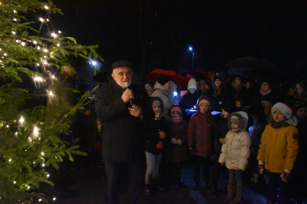 Mężczyzna trzymający mikrofon, z lewej strony drzewko świąteczne